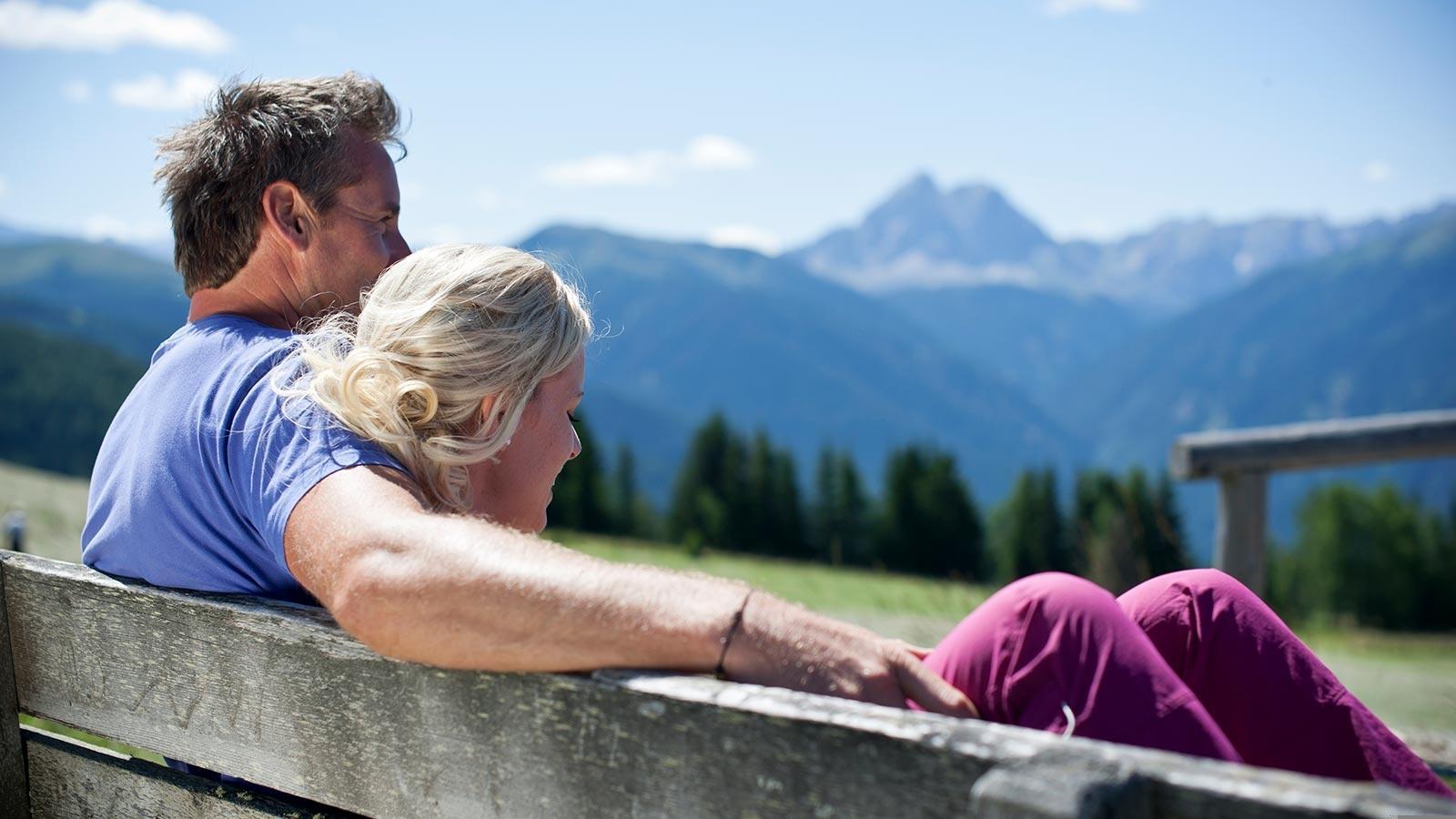 ein Paar sitzt auf einer Holzbank und genießt das Panorama von Meransen und des Pustertals